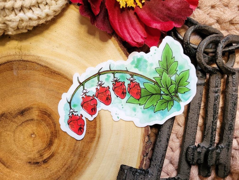 May include: A watercolor sticker featuring a vine with red heart-shaped flowers. The vine is green with leaves and the hearts are a vibrant red. The sticker is on a wooden background.