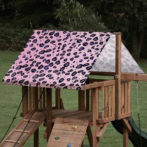 May include: Pink and purple leopard print canopy for a wooden playset. The canopy is attached to the playset with ropes.