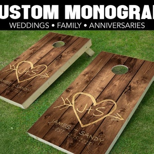 May include: Two wooden cornhole boards with a rustic brown wood grain finish. Each board has a heart with the initials "J+S" and the text "James + Sandy Est. 10.15.2023" in gold.