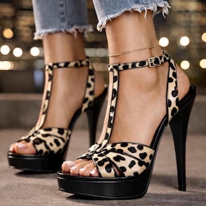 May include: High-heeled platform sandals with a leopard print design. The open-toe shoes have a black platform sole and a thin ankle strap with a buckle. The heels are black and slender.