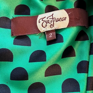 Puede incluir: Primer plano del forro de una prenda. El forro es una tela verde vibrante con un patr&oacute;n de semic&iacute;rculos negros. Una etiqueta marr&oacute;n con el texto "Eva Franco" y el n&uacute;mero "2" est&aacute; adherida al forro.