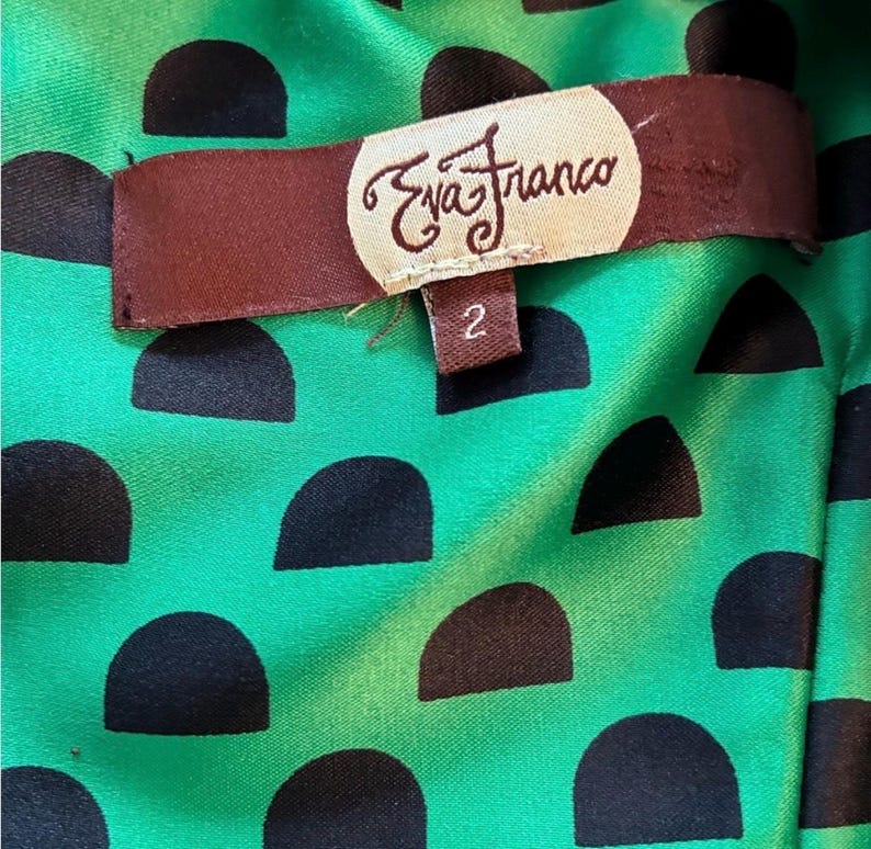Puede incluir: Primer plano del forro de una prenda. El forro es una tela verde vibrante con un patr&oacute;n de semic&iacute;rculos negros. Una etiqueta marr&oacute;n con el texto "Eva Franco" y el n&uacute;mero "2" est&aacute; adherida al forro.