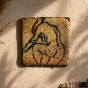 May include: Square ceramic wall art featuring a black line drawing of a figure in a seated pose. The artwork has a textured, mottled surface with a blend of brown, tan, and green hues. The edges of the artwork are darker, creating a framed effect.