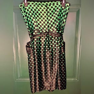 Puede incluir: Vestido sin tirantes con estampado geom&eacute;trico negro y verde. El vestido tiene un corpi&ntilde;o ajustado, una cintura definida con un cintur&oacute;n a juego y una falda a la rodilla. La tela tiene un aspecto brillante.