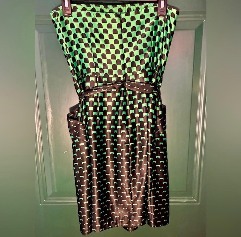 Puede incluir: Vestido sin tirantes con estampado geom&eacute;trico negro y verde. El vestido tiene un corpi&ntilde;o ajustado, una cintura definida con un cintur&oacute;n a juego y una falda a la rodilla. La tela tiene un aspecto brillante.