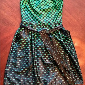 Puede incluir: Vestido sin tirantes con un estampado geom&eacute;trico negro y verde. El vestido presenta un corpi&ntilde;o ajustado y una falda acampanada, ce&ntilde;ida a la cintura con un cintur&oacute;n negro a juego. La tela tiene un brillo brillante.