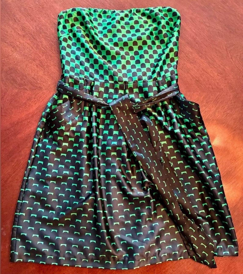 Puede incluir: Vestido sin tirantes con un estampado geom&eacute;trico negro y verde. El vestido presenta un corpi&ntilde;o ajustado y una falda acampanada, ce&ntilde;ida a la cintura con un cintur&oacute;n negro a juego. La tela tiene un brillo brillante.