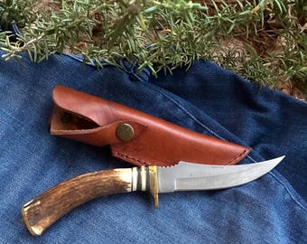Cuchillo de caza americano antiguo con mango de asta y funda de cuero.