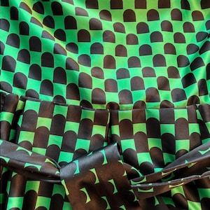 Puede incluir: Primer plano de una tela estampada verde y negra. El patr&oacute;n consiste en formas de semic&iacute;rculo negro dispuestas en una cuadr&iacute;cula sobre un fondo verde brillante. Un cintur&oacute;n de tela a juego es visible en la parte inferior, agregando un elemento de dise&ntilde;o cohesivo. La tela parece ser sat&eacute;n o seda.