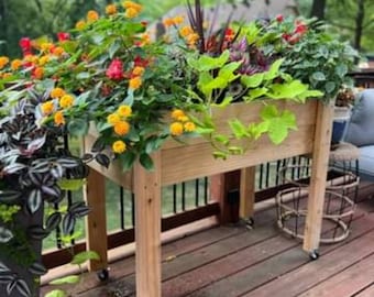 Op de afbeelding: Een verhoogd houten plantenbak met wielen, gevuld met kleurrijke bloemen. De bak is gemaakt van natuurlijk hout en heeft een rustieke uitstraling. De bloemen bloeien volop en voegen een vleugje kleur toe aan de tuin.