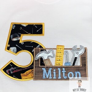 May include: A white t-shirt with a black and yellow number 5 and a brown toolbox with tools and the name Milton in blue.