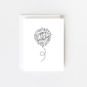 May include: A black and white greeting card with a balloon illustration. The balloon is surrounded by a wreath of flowers and leaves. The text inside the balloon reads "happy birthday".