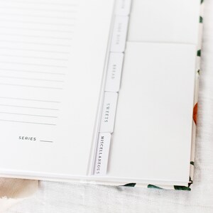 May include: A white recipe book with tabs for different categories: Bread, Sweets, Miscellaneous. The book has a white cover with the word "SERIES" printed on the front.