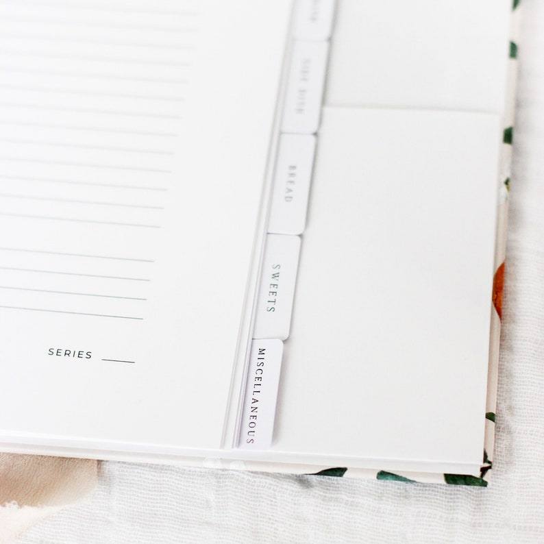 May include: A white recipe book with tabs for different categories: Bread, Sweets, Miscellaneous. The book has a white cover with the word "SERIES" printed on the front.