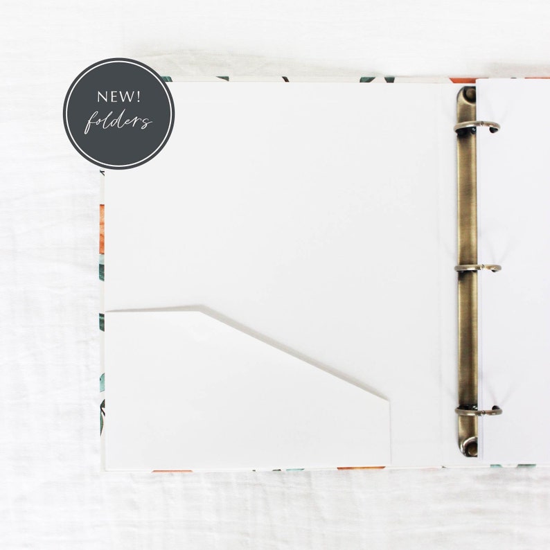 May include: A white binder with a floral pattern on the cover. The binder has a brass ring mechanism and a white pocket folder inside. The text "NEW! folders" is written on a gray circle.