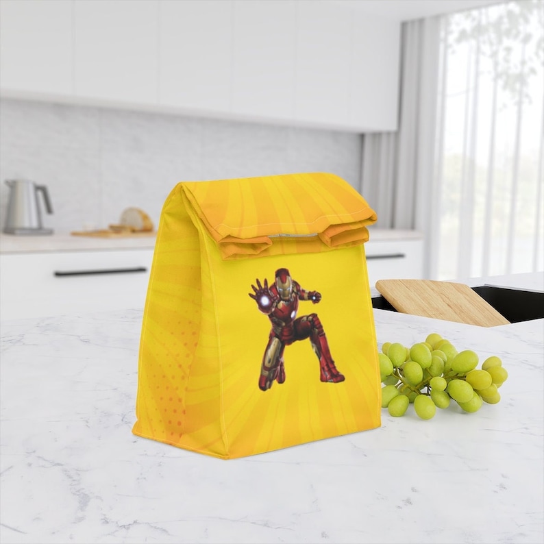 Puede incluir: Bolsa de almuerzo amarilla con un personaje de Iron Man rojo y plateado. La bolsa tiene una parte superior plegable con cierre de velcro.