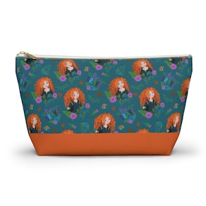 May include: A teal zippered pouch with a repeating pattern of a cartoon girl with red hair, flowers, and the words "be brave". The pouch has a brown bottom.