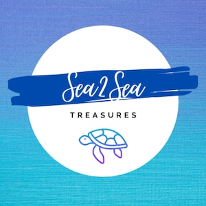 May include: A white circle with a blue brushstroke across the top. The text "Sea 2 Sea Treasures" is written in white cursive script on the blue brushstroke. A blue and purple outline of a sea turtle is in the center of the circle.