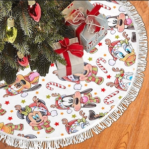May include: White Christmas tree skirt with a white fringe border. The skirt features a repeating pattern of Mickey Mouse, Minnie Mouse, Donald Duck, and Goofy wearing Santa hats and holding candy canes. The background is white with red stars.