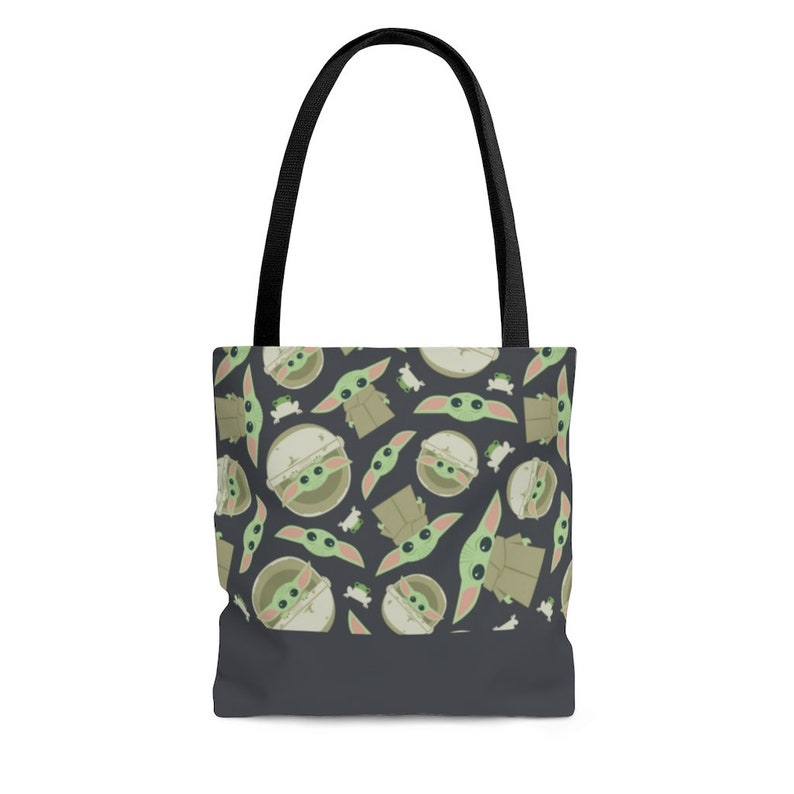 Puede incluir: Una bolsa de mano de color gris oscuro con asas negras presenta un patr&oacute;n repetido de personajes de dibujos animados verdes y marrones con ojos grandes.