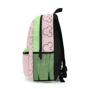 May include: A pink and green backpack with a black zipper and a pattern of black Mickey Mouse heads. The backpack has a mesh pocket on the side.