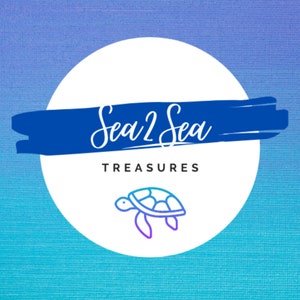 May include: A white circle with a blue brushstroke across the top. The text "Sea 2 Sea Treasures" is written in white cursive script on the blue brushstroke. A blue and purple outline of a sea turtle is in the center of the circle.