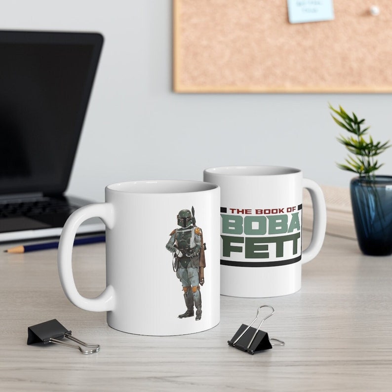 May include: Two white ceramic mugs with a Star Wars theme. One mug features a graphic of Boba Fett, the other mug has the text "The Book of Boba Fett".