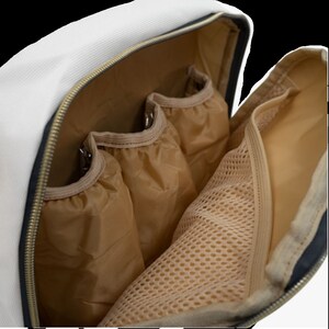 May include: A white canvas backpack with a black zipper and a brown mesh pocket. The backpack has three interior pockets with brown fabric.