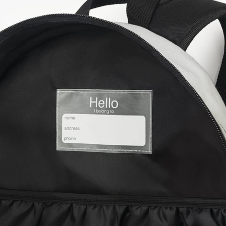 Puede incluir: Mochila negra con una etiqueta transparente de pl&aacute;stico que dice "Hello I belong to" con espacios para el nombre, la direcci&oacute;n y el n&uacute;mero de tel&eacute;fono.
