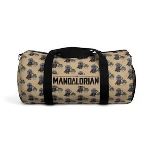 Puede incluir: Una bolsa de lona de color beige con correas negras y un patr&oacute;n repetido de un peque&ntilde;o personaje alien&iacute;gena verde que sostiene un peque&ntilde;o personaje gris. La bolsa tiene el texto "THE MANDALORIAN" impreso en negro en la parte delantera.