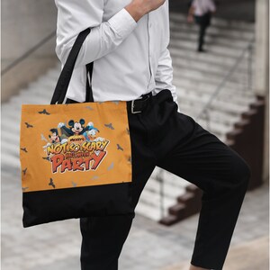 May include: A black and yellow tote bag with a Mickey Mouse Halloween design. The bag features Mickey Mouse, Donald Duck, and Goofy dressed in Halloween costumes. The text on the bag reads "Mickey's Not-So-Scary Halloween Party".