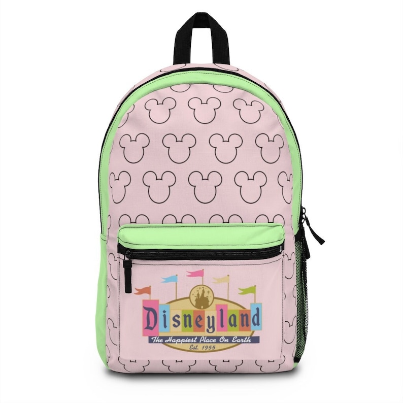 May include: A pink and green backpack with a black zipper and a white outline of Mickey Mouse ears repeated on the front and back. The front pocket has a colorful Disneyland logo with the text "The Happiest Place On Earth" and "Est. 1955".