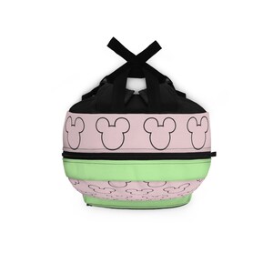 May include: A black, green, and pink backpack with a repeating pattern of Mickey Mouse ears. The backpack has a black zipper and adjustable straps.