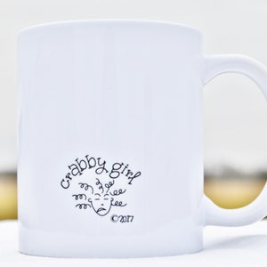 May include: White ceramic mug with a black design that says "Crabby Girl" with a cartoon face and the copyright symbol 2017.