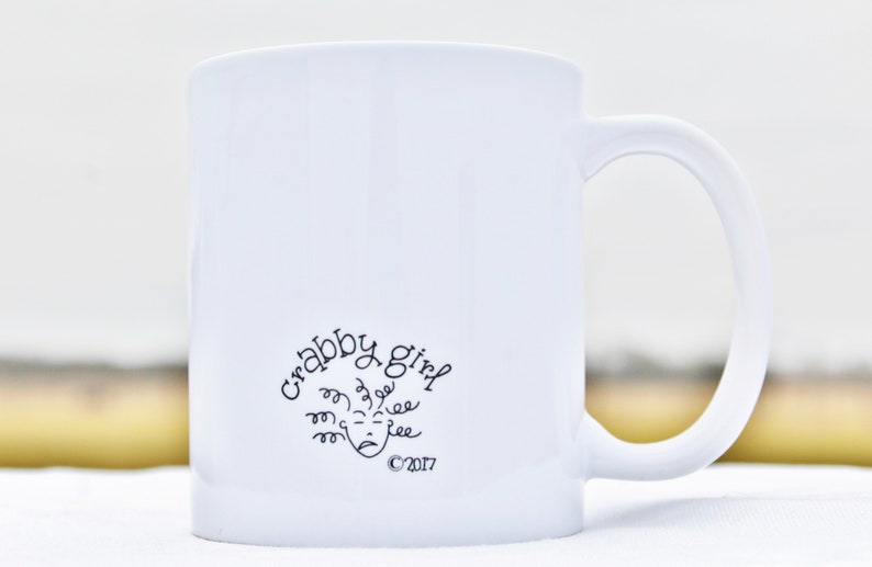May include: White ceramic mug with a black design that says "Crabby Girl" with a cartoon face and the copyright symbol 2017.