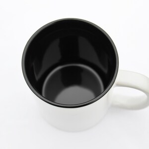 May include: A white ceramic mug with a black interior and a black rim. The mug has a handle on the right side.