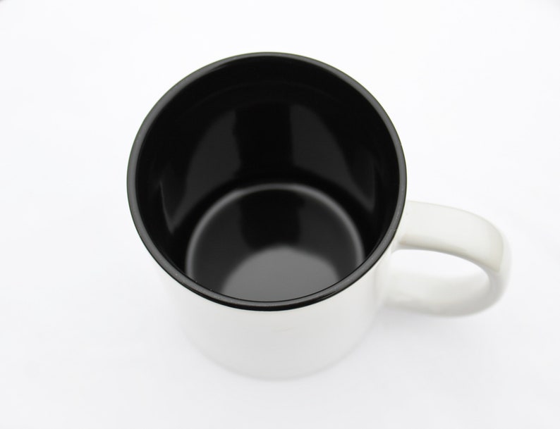 May include: A white ceramic mug with a black interior and a black rim. The mug has a handle on the right side.