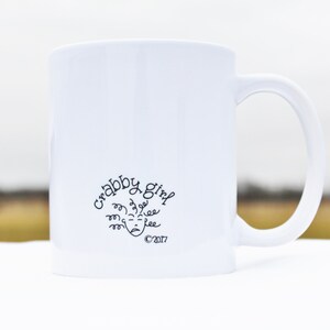 May include: White ceramic coffee mug with a black design that says "Crabby Girl" with a cartoon face and the copyright symbol 2017.