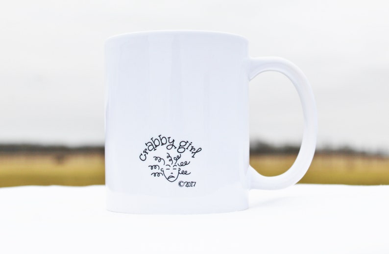 May include: White ceramic coffee mug with a black design that says "Crabby Girl" with a cartoon face and the copyright symbol 2017.