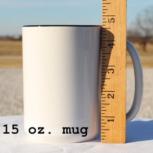 May include: A white 15 oz. mug with a black rim. The mug is next to a wooden ruler with markings in inches.
