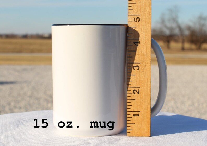 May include: A white 15 oz. mug with a black rim. The mug is next to a wooden ruler with markings in inches.