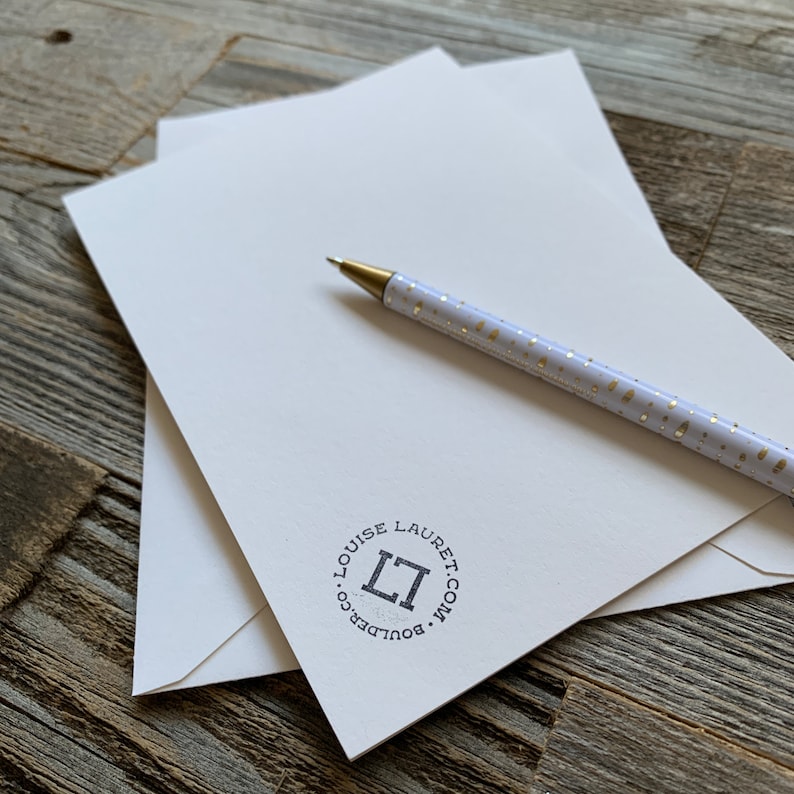 May include: White stationery with a gold pen and a black and white logo that says "Louise Lauret.com - Boulder, CO" in a circle.