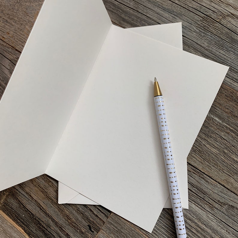May include: A blank white card with a white pen with gold dots on it. The card is folded in half and the pen is lying on top of the card.