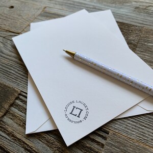 May include: Ivory stationery set with a gold-tipped pen. The stationery includes a stack of envelopes and a matching card, with a circular logo that reads "LOUISE LAURET. BOULDER.CO". The pen is white with gold polka dots.
