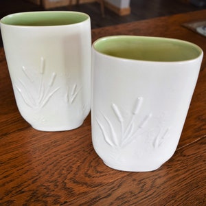May include: Two white ceramic vases with a green rim and embossed reeds design.