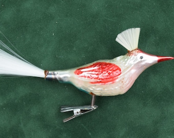 May include: A vintage glass bird ornament with a white body, red breast, and a red beak. The bird has a white crest and tail, and a metal clip for hanging. The ornament is likely for Christmas or holiday decor.