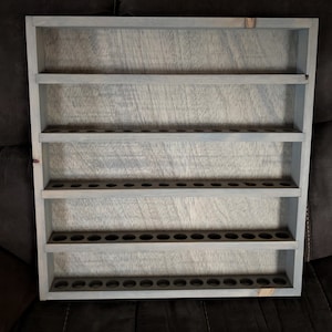 May include: A gray wooden shelf with five shelves and multiple small holes on each shelf. The shelf is designed to hold small bottles or tubes.