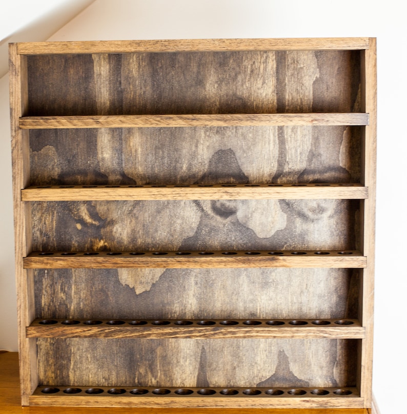 May include: A wooden shelf unit with five shelves and a row of small holes along the bottom of each shelf. The shelves are stained a dark brown color.
