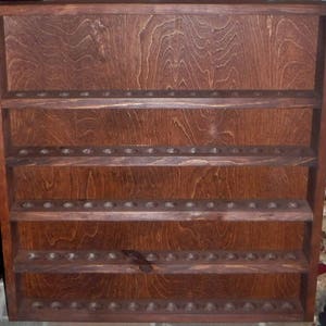 May include: A dark brown wooden wall shelf with four shelves. Each shelf has multiple small holes for storing items. The shelf is made of wood with a natural grain pattern.