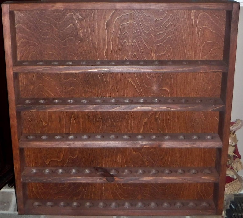 May include: A dark brown wooden wall shelf with four shelves. Each shelf has multiple small holes for storing items. The shelf is made of wood with a natural grain pattern.